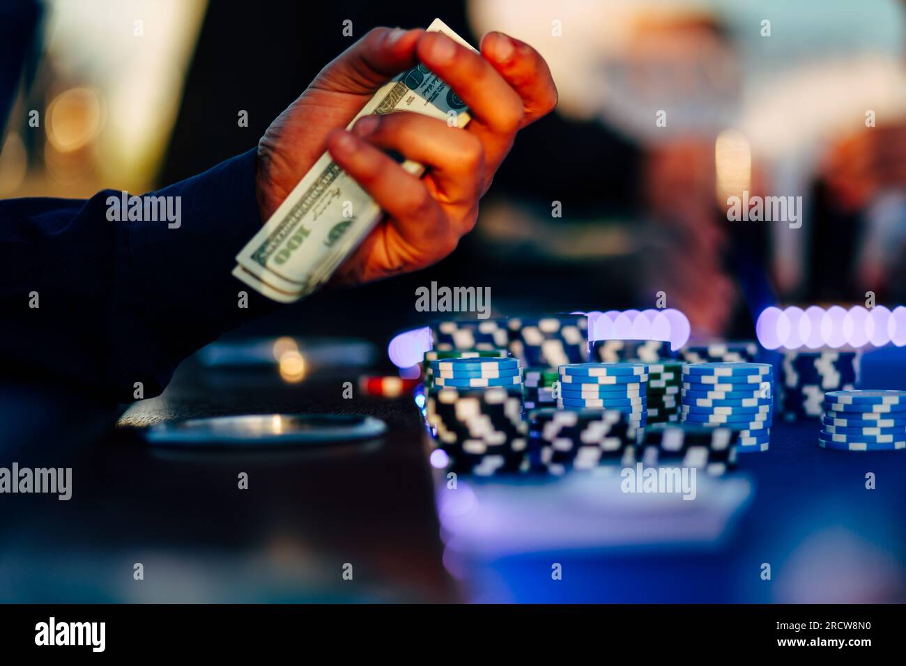 un giocatore d'azzardo seduto vicino alla roulette con dollari in contanti nelle sue mani e sul tavolo ci sono delle fiche da casinò. Foto Stock