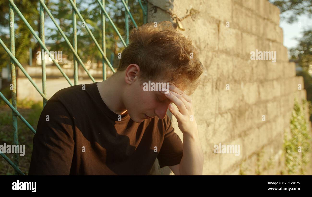 Uomo biondo all'aperto, che tiene la testa ed esprime disagio Foto Stock