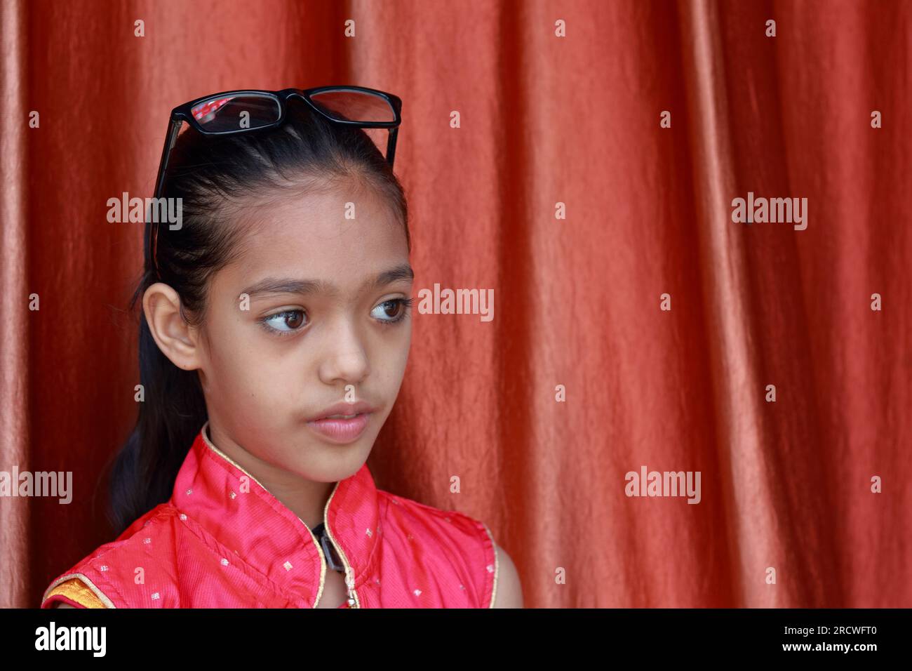 Una piccola bella ragazza indiana che si sporca con gli occhiali in varie pose in abito rosso. Foto Stock