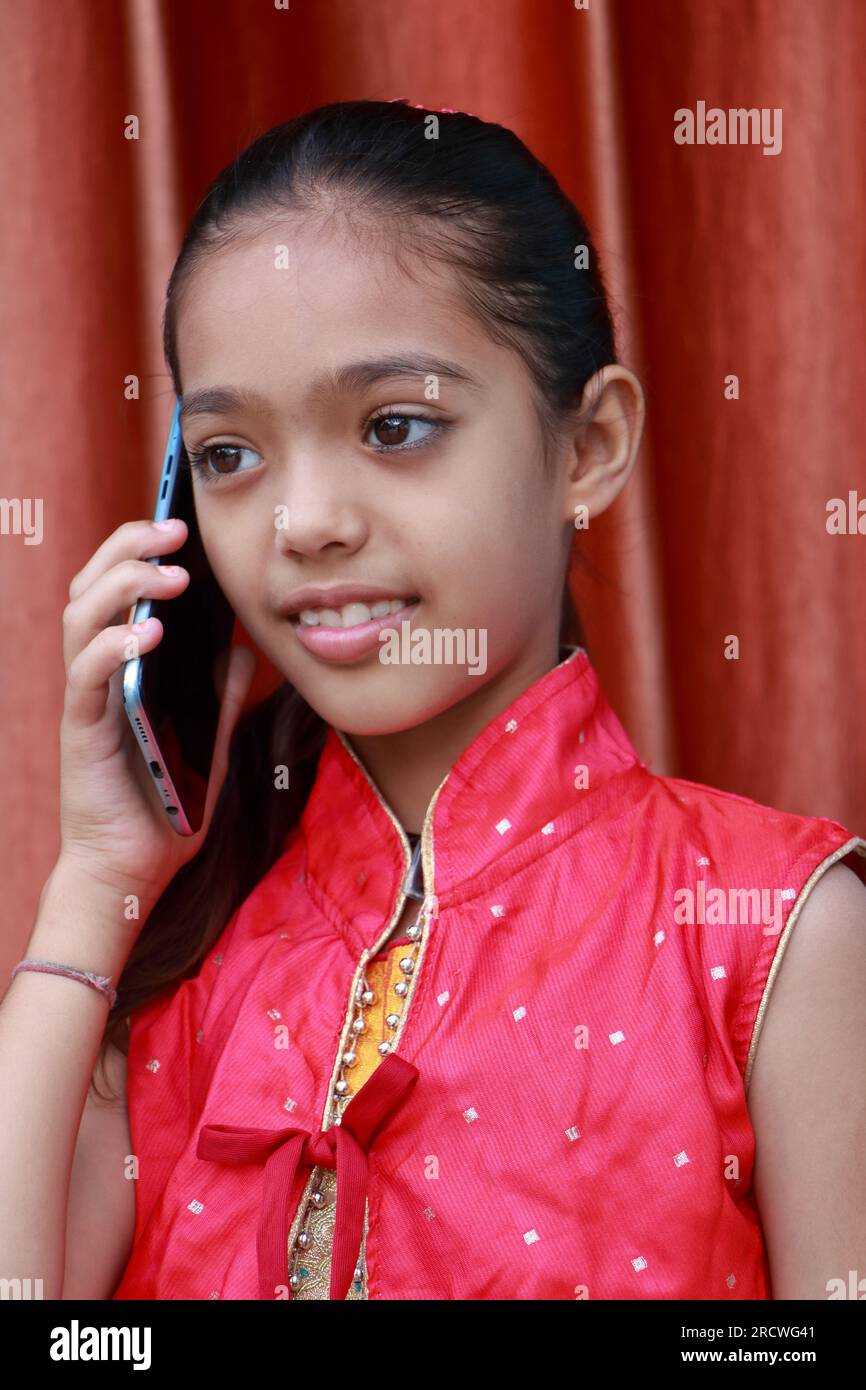 Una piccola bella ragazza indiana che parla su un telefono cellulare in varie pose con vestito rosso. Foto Stock