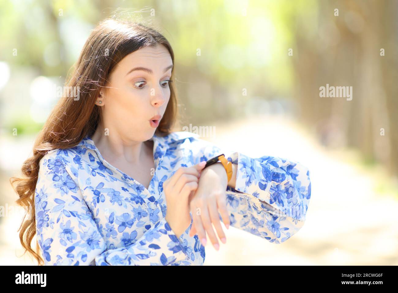 Una donna sorpresa che controlla uno smartwatch che cammina in un parco Foto Stock