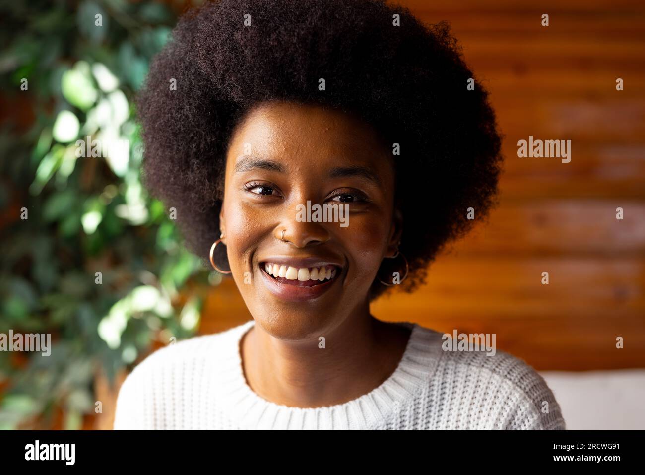 Ritratto di una donna afroamericana con afro e anello nasale sorridente in una stanza soleggiata Foto Stock
