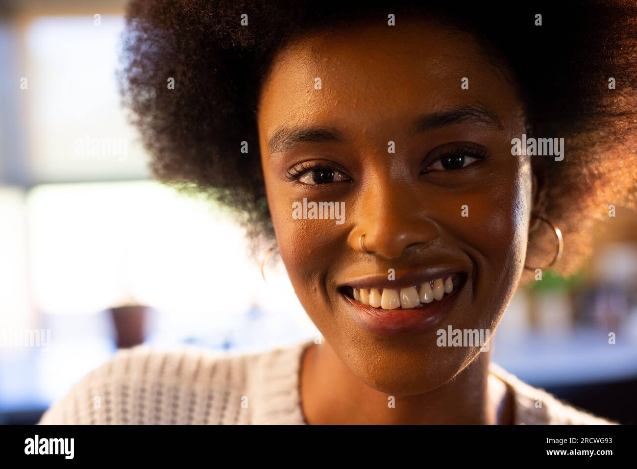 Ritratto di una donna afroamericana con afro e anello nasale sorridente nella soleggiata cucina Foto Stock