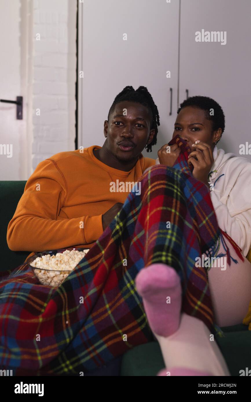 Coppia afroamericana spaventata che si rilassa a casa guardando un film spaventoso con popcorn Foto Stock