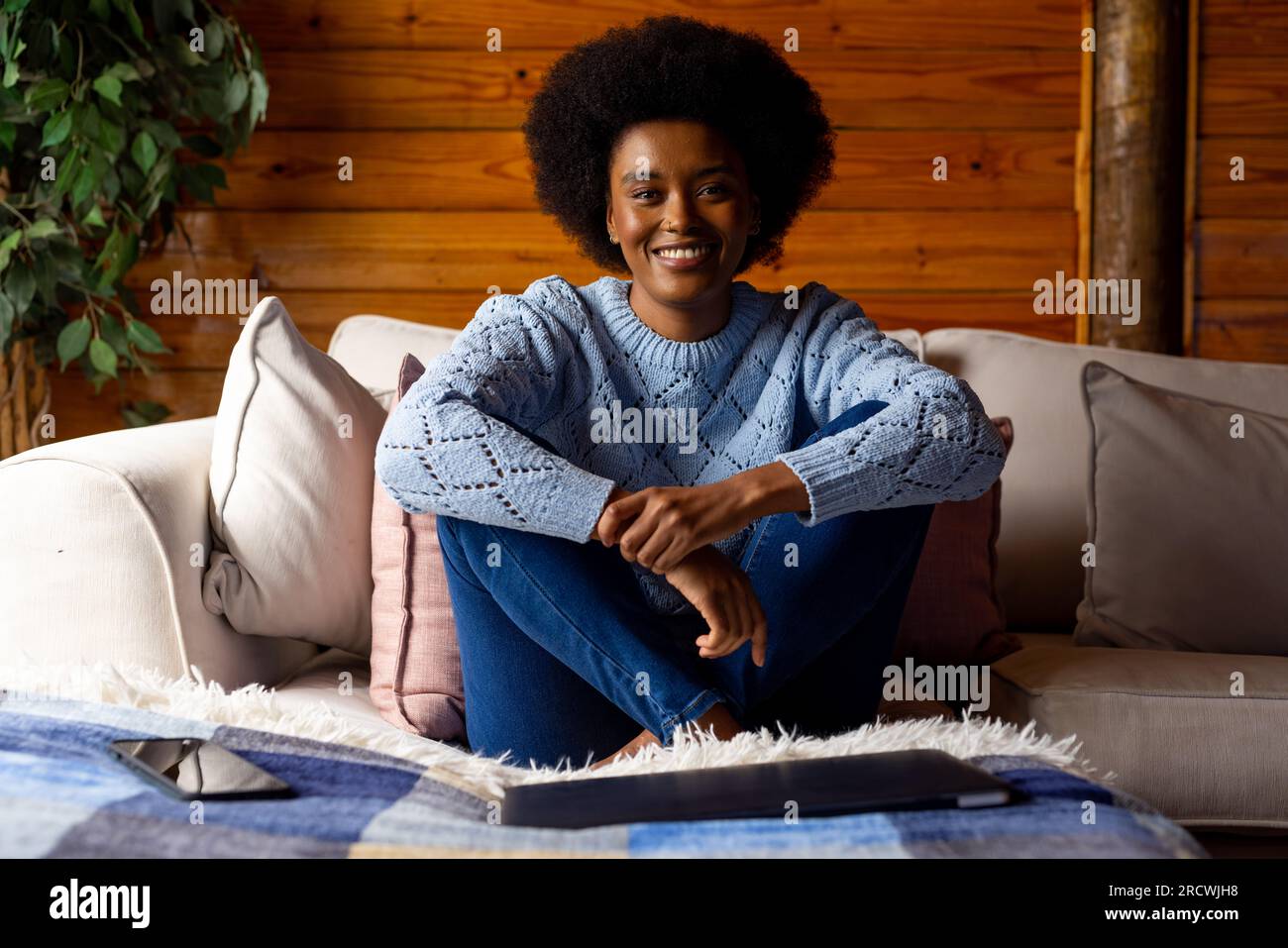 Ritratto di una felice donna afroamericana seduta sul divano nel soggiorno di una capanna di legno Foto Stock