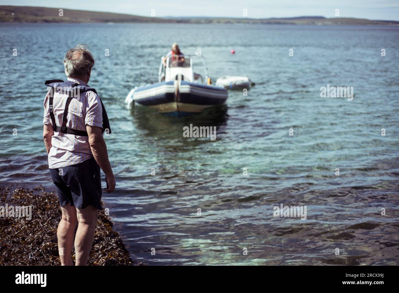 Un uomo più anziano guarda una donna che guida una barca a motore al molo Foto Stock