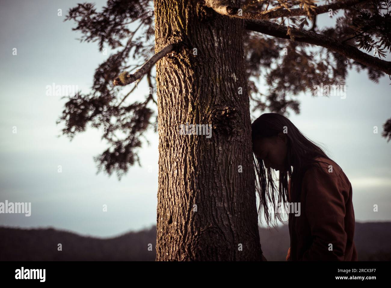La persona androgina appoggia la testa sull'albero Foto Stock