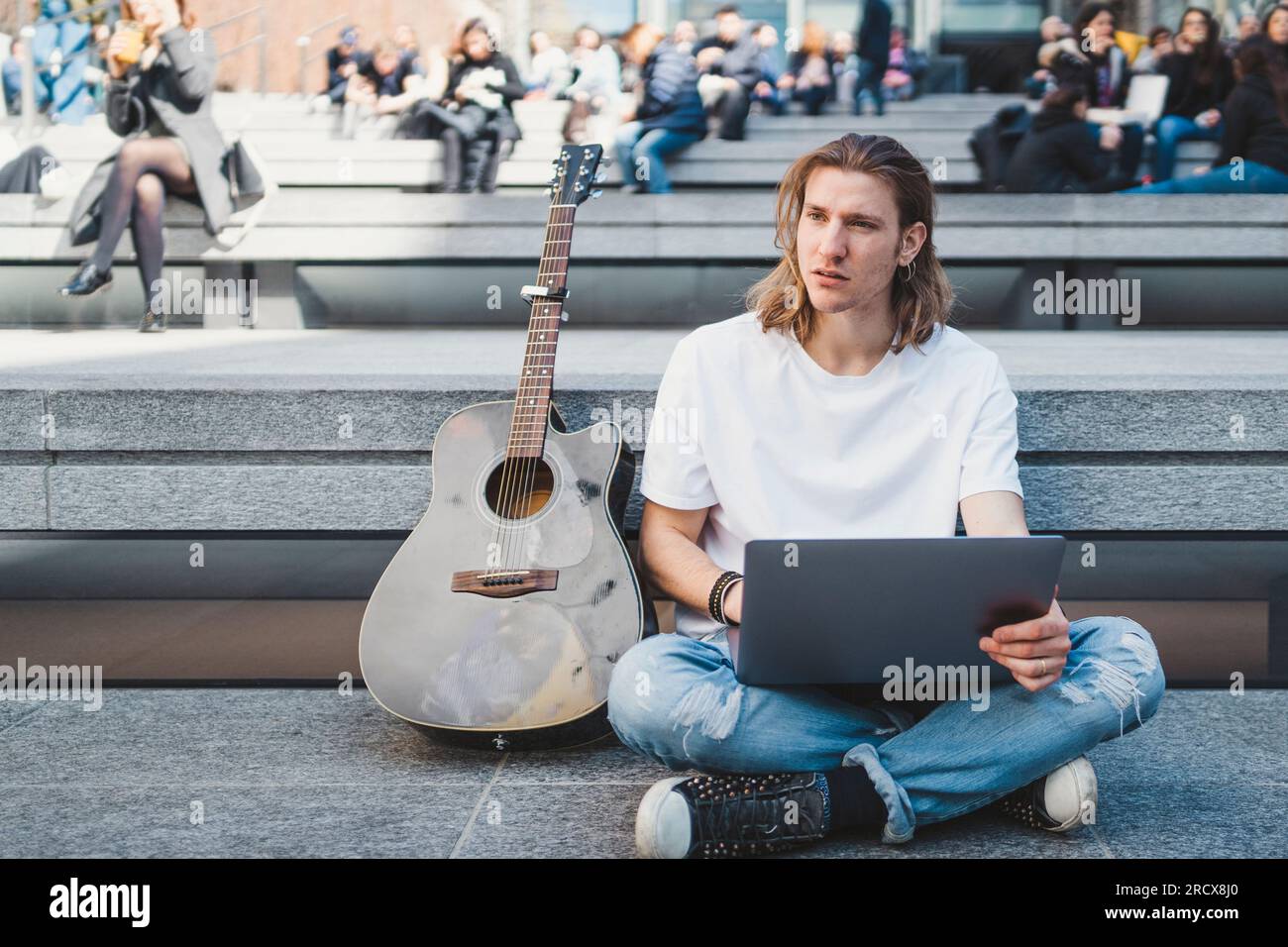 uomo bianco che usa un notebook all'aperto accanto alla sua chitarra acustica Foto Stock