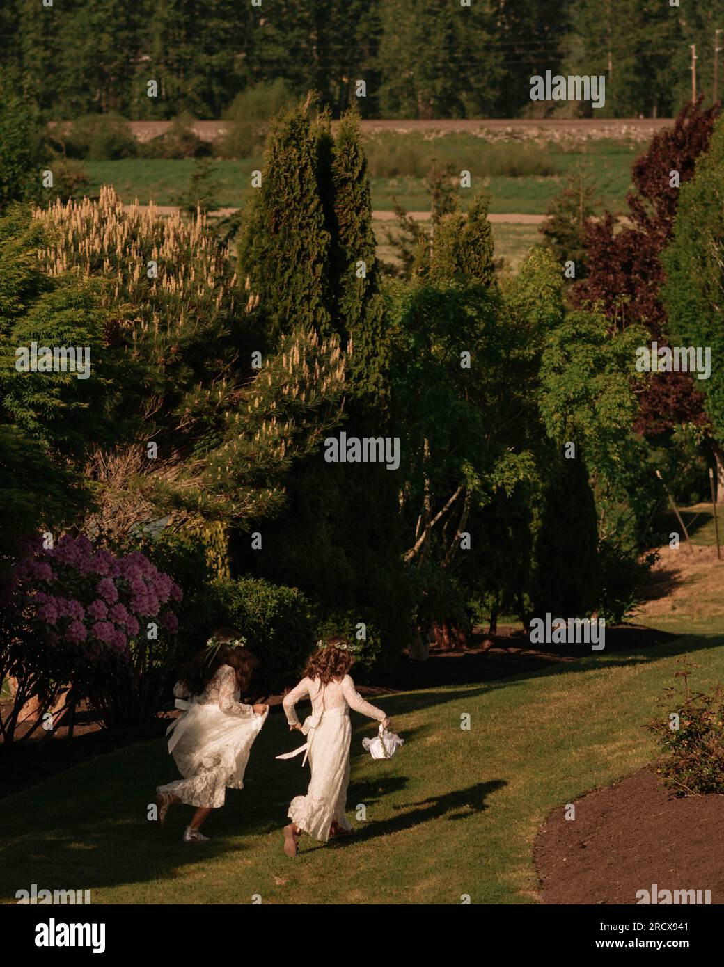 due ragazze di fiori corrono in un soleggiato matrimonio in giardino. Foto Stock
