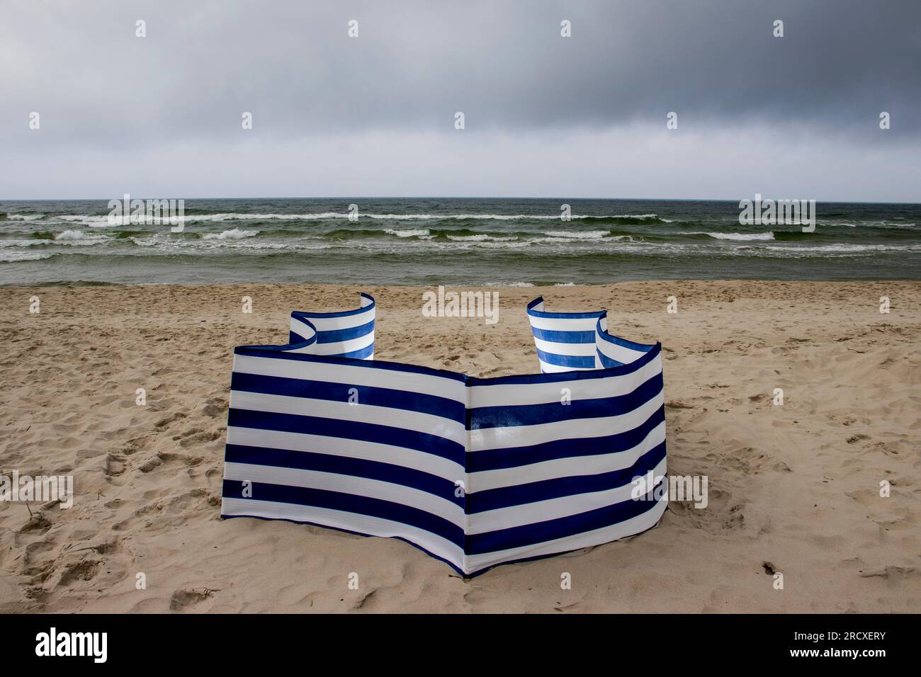 Windbreak. In una giornata nuvolosa in spiaggia, sperando in un sole. Livelli del personale. Nuvole e maggio e uno schermo a strisce sulla spiaggia. Foto Stock