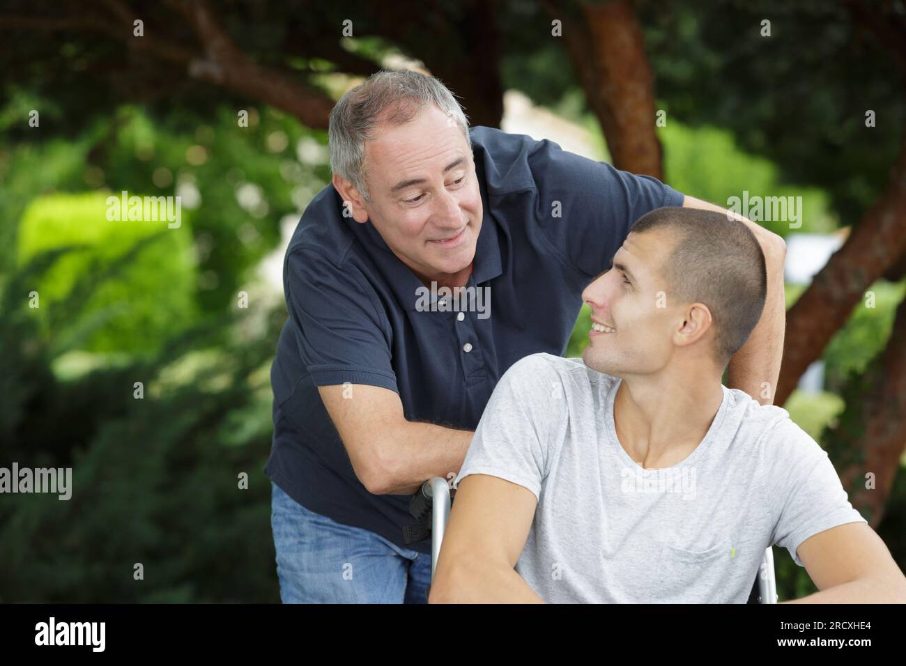 uomo che spinge il figlio in sedia a rotelle Foto Stock