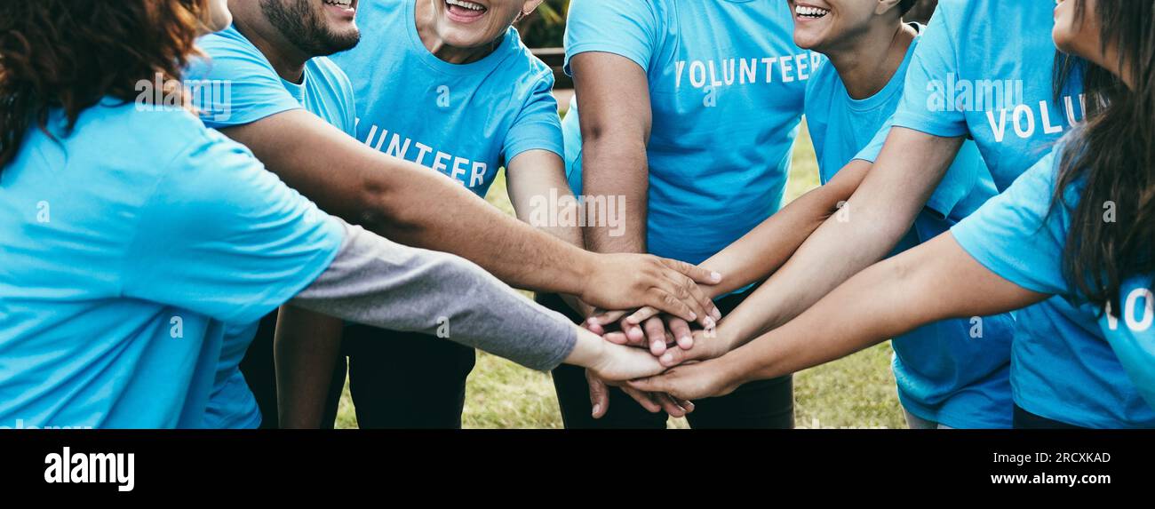 Felice gruppo di volontari che si accatastano le mani per festeggiare insieme all'aperto - concetto di lavoro di squadra e supporto di beneficenza - Focus sui volti posteriori Foto Stock