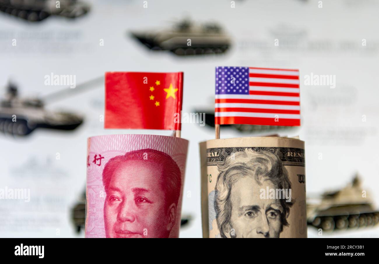 Un rotolo di USD e Yuan cinese con le bandiere nazionali di ogni paese di fronte a un background militare. Una spesa militare, una competizione, una corsa agli armamenti. Foto Stock