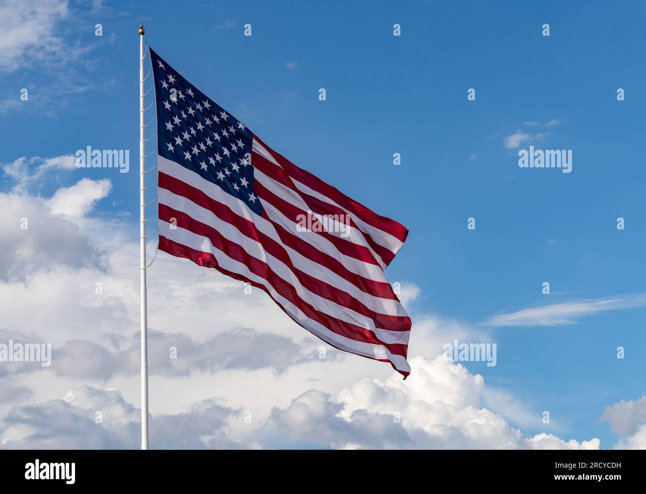 Stelle e strisce con bandiera USA di grandi dimensioni che soffiano nel vento con interessanti nuvole dietro nel cielo blu Foto Stock