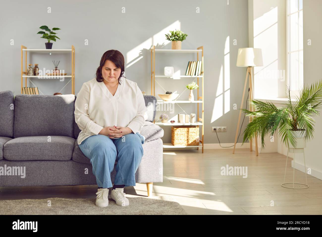 Donna sovrappeso depressa seduta sul divano a casa Foto Stock