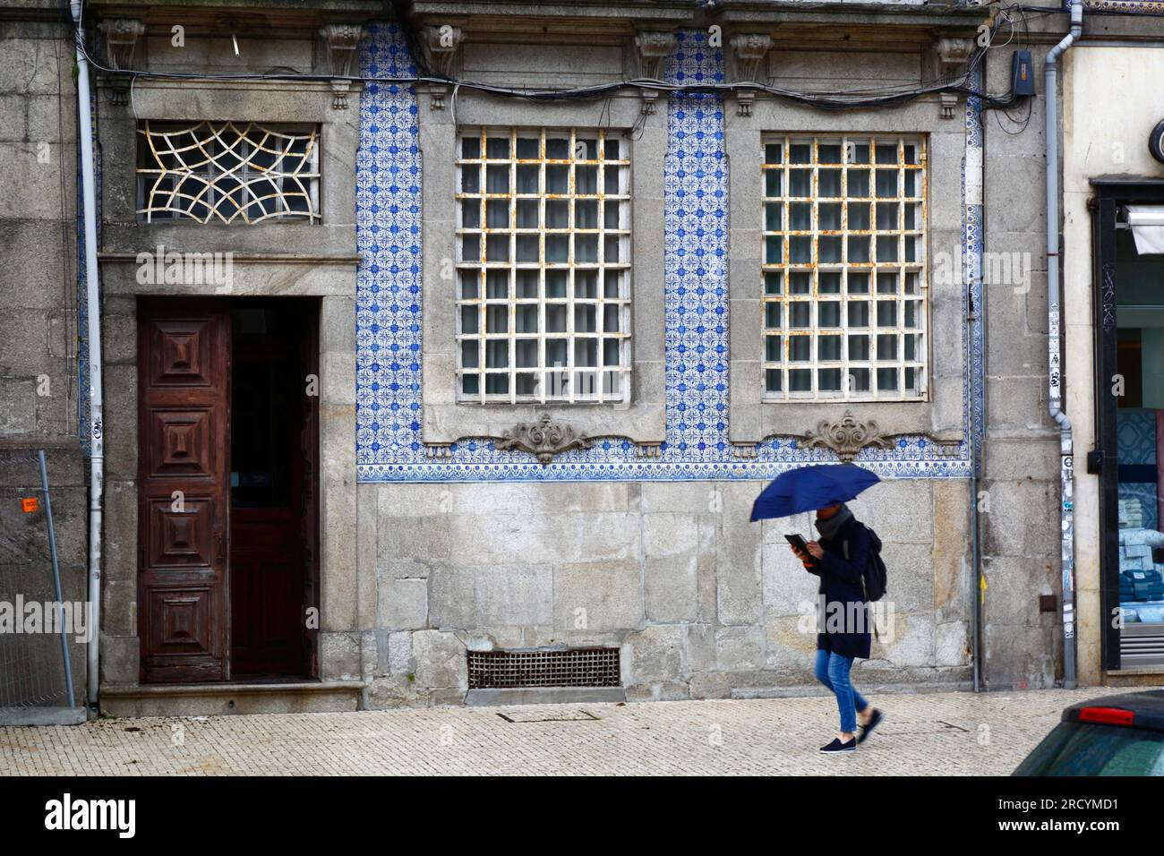 Persona che legge un libro sotto un ombrello che cammina davanti a una vecchia casa di typìcal accanto alla chiesa di Igreja do Carmo, Porto / Oporto, Portogallo Foto Stock
