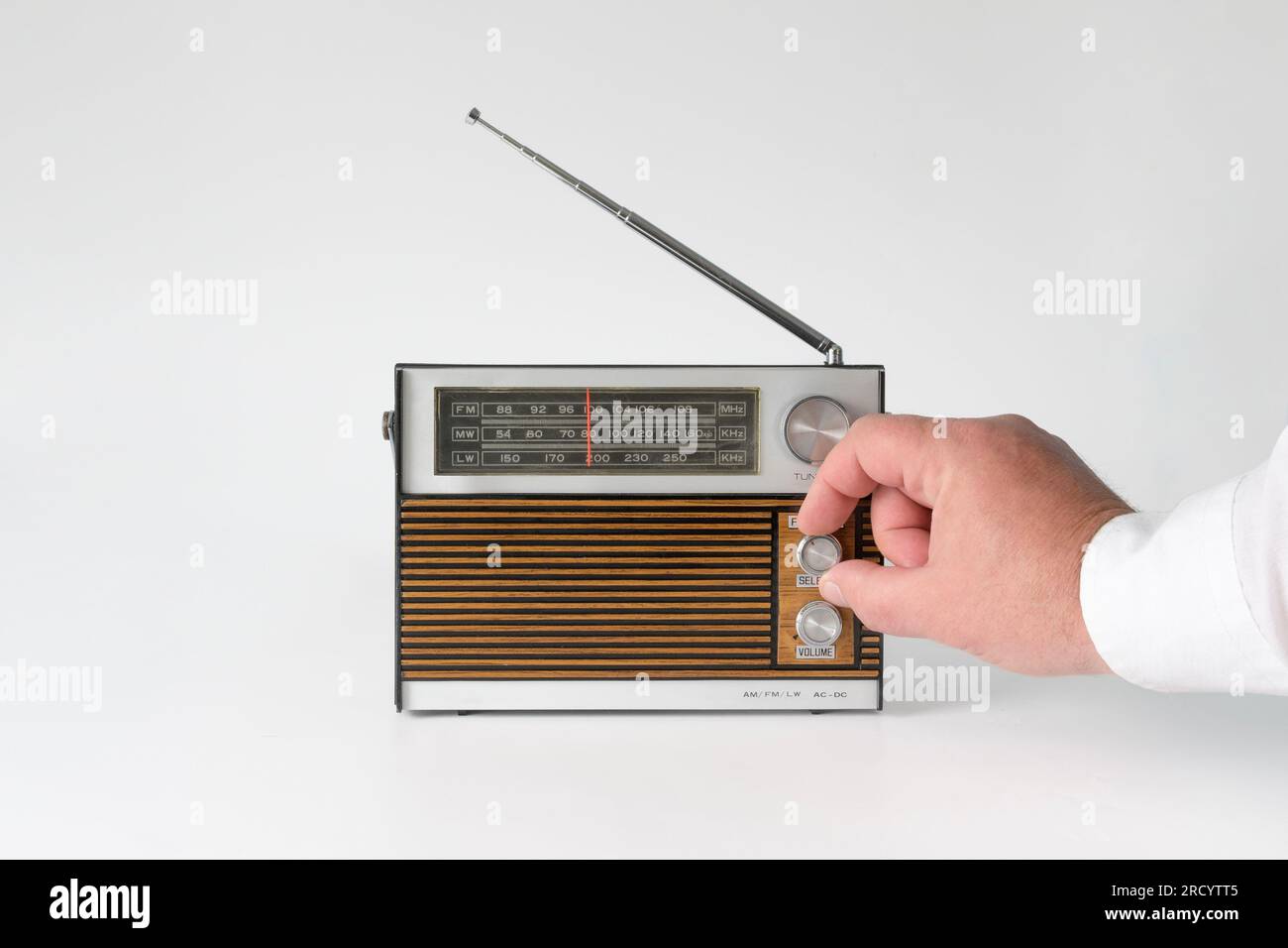La mano di un uomo torce l'ambientazione delle onde. Radio autentica degli anni '70 Isolato su sfondo bianco. Tracce di tempo e segni sul caso Foto Stock