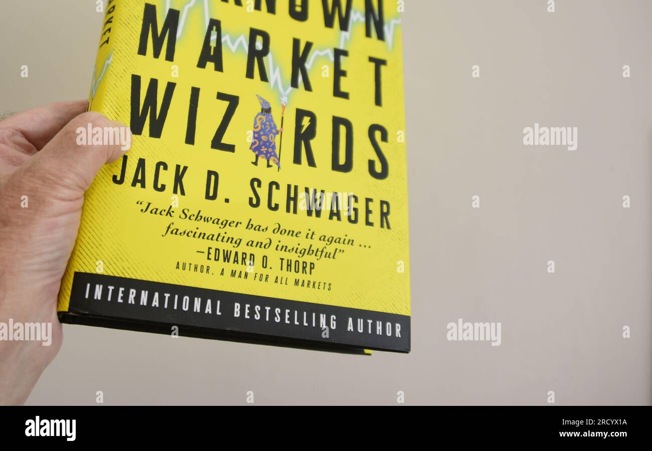 La mano sinistra di un uomo caucasico contiene una copia del libro "Market Wizards" di Jack D. Schwager, i migliori commercianti che non hai mai sentito parlare del tema Foto Stock