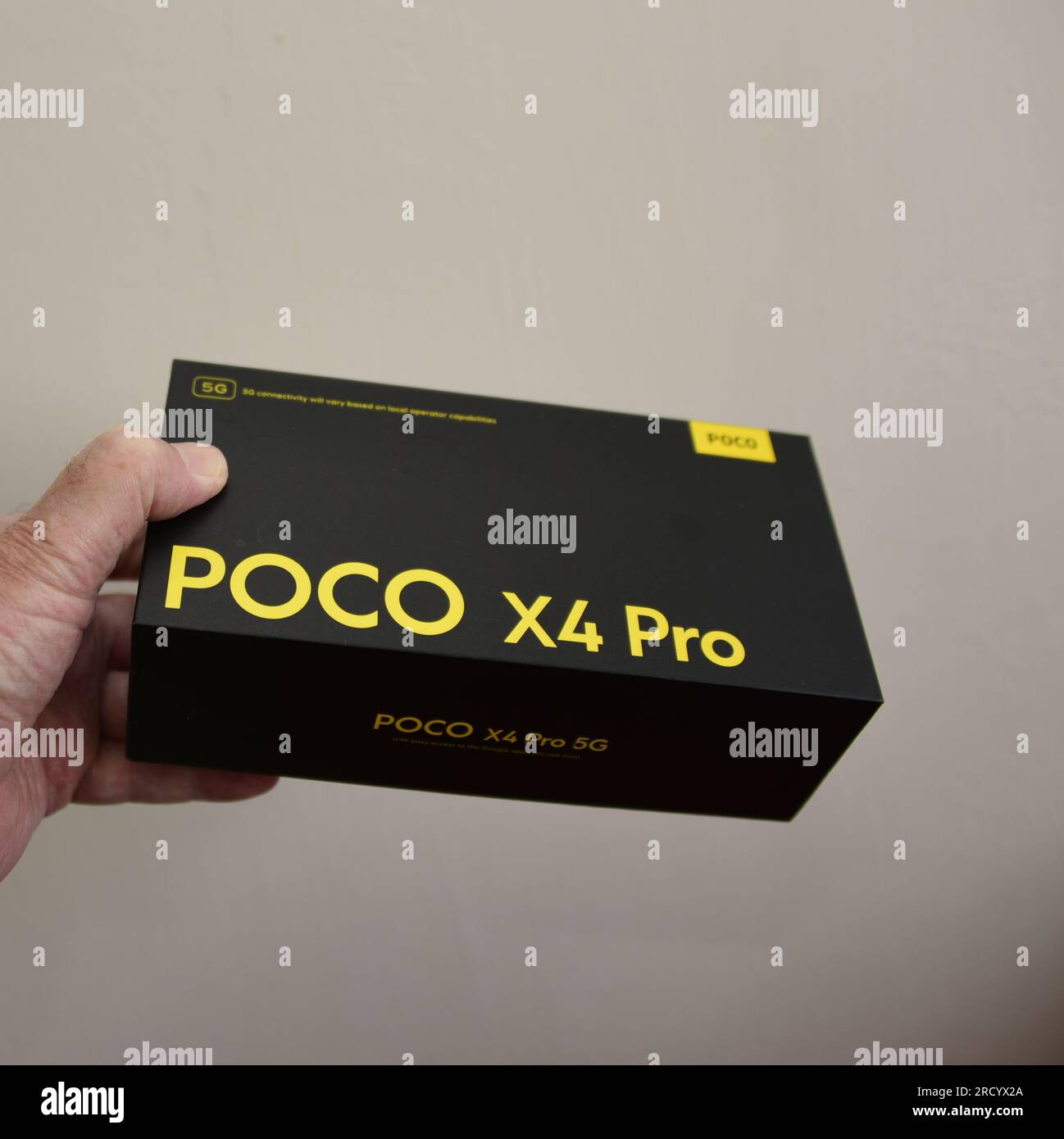 La mano sinistra di un uomo caucasico tiene la scatola per un telefono cellulare 5G di marca poco X4 Pro Foto Stock
