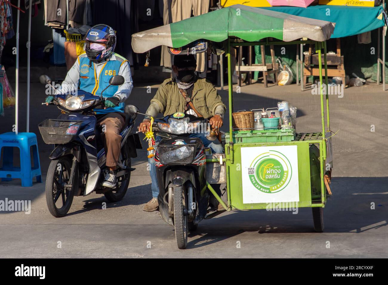 SAMUT PRAKAN, THAILANDIA, 07 2023 FEBBRAIO, un distributore di gelati cavalca una moto a tre ruote su una strada con stand Foto Stock