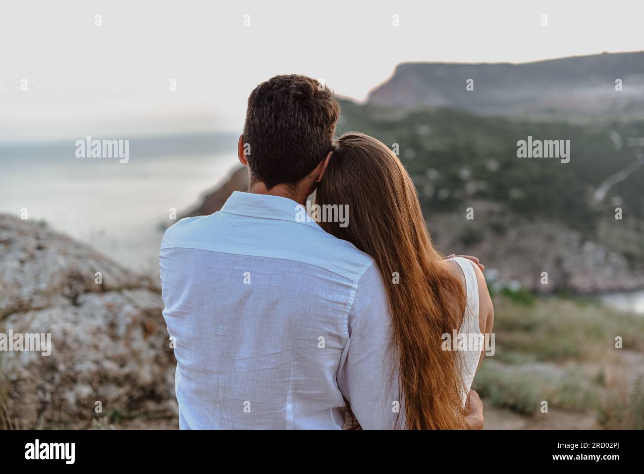 Bella giovane e amorevole coppia uomo dall'aspetto mediorientale e una donna caucasica abbracciano, baciano all'alba. Storia d'amore all'aperto. Foto Stock