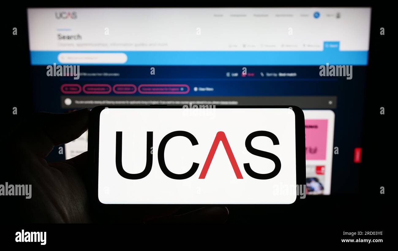 Persona che possiede il cellulare con il logo del servizio di ammissione alle università e ai college (UCAS) sullo schermo davanti alla pagina Web. Concentrarsi sul display del telefono. Foto Stock