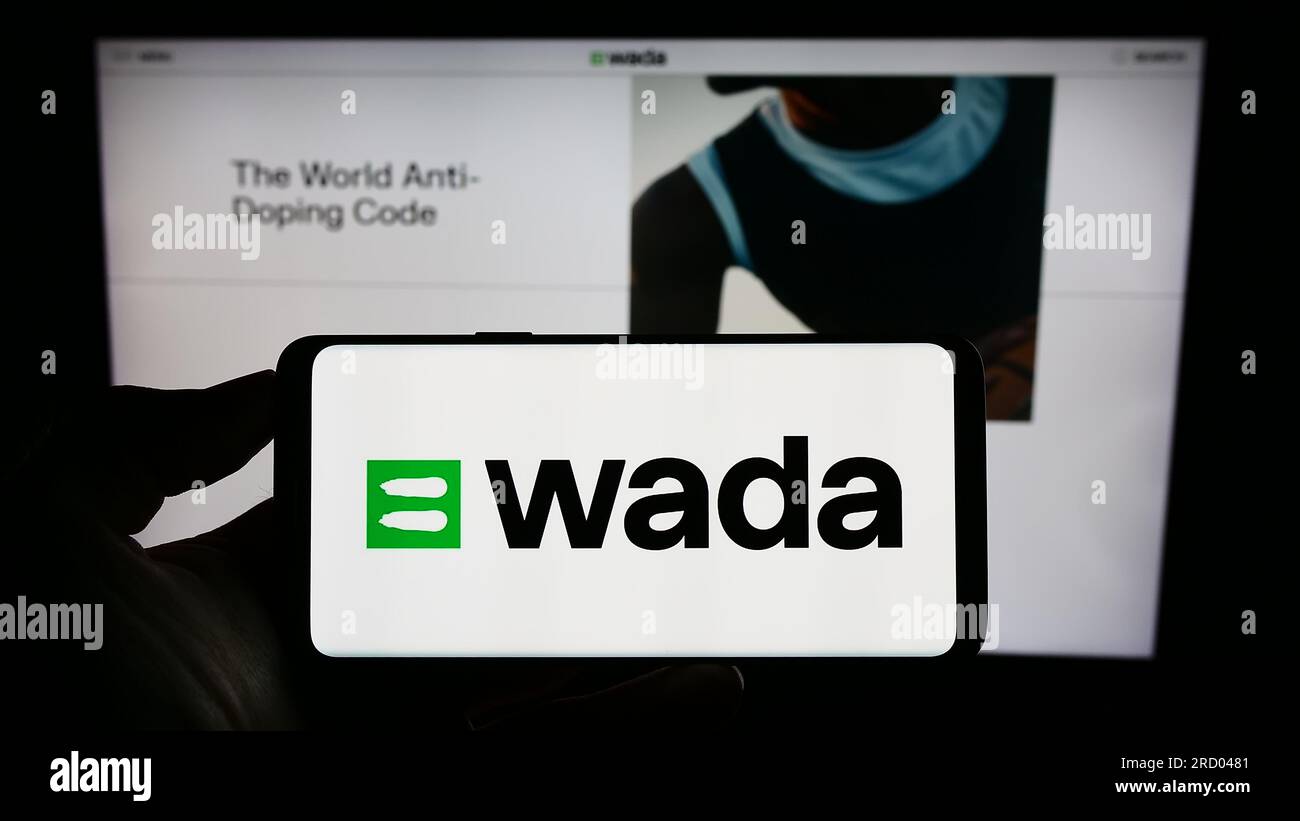 Persona che possiede un telefono cellulare con il logo dell'organizzazione World Anti-doping Agency (WADA) sullo schermo davanti alla pagina web. Concentrarsi sul display del telefono. Foto Stock
