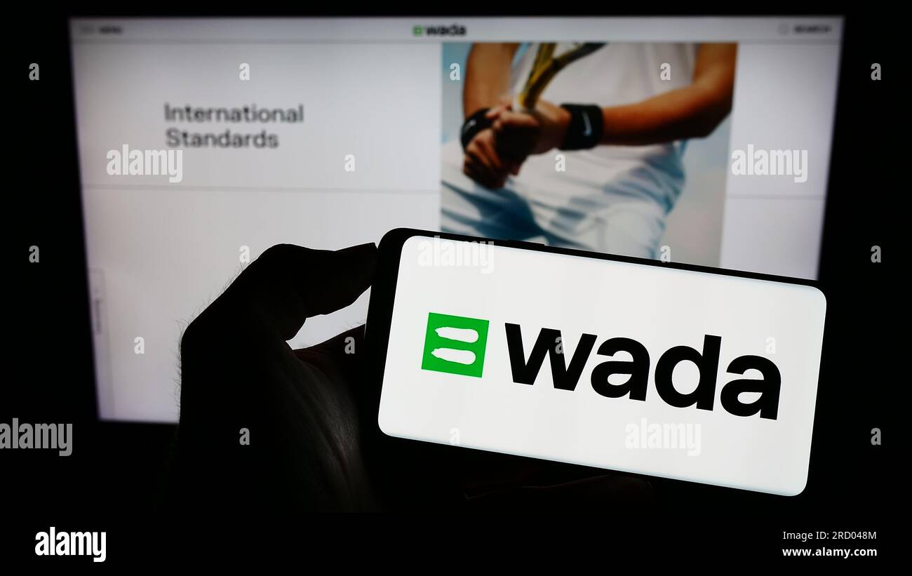 Persona che detiene il cellulare con il logo dell'organizzazione World Anti-doping Agency (WADA) sullo schermo davanti alla pagina web. Concentrarsi sul display del telefono. Foto Stock