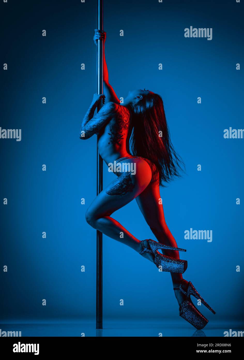 Giovane donna nuda sexy pole dance. Luci al neon blu e rosse. Tatuaggio sul corpo. Foto Stock