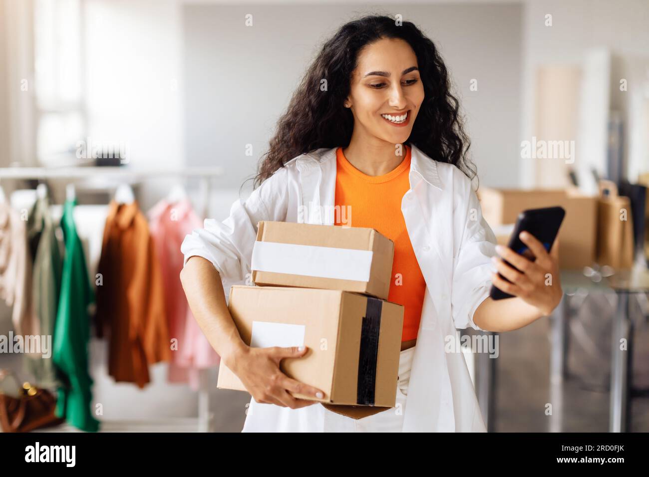 Fashion Designer Messaging su cellulare in posa con le scatole in negozio Foto Stock