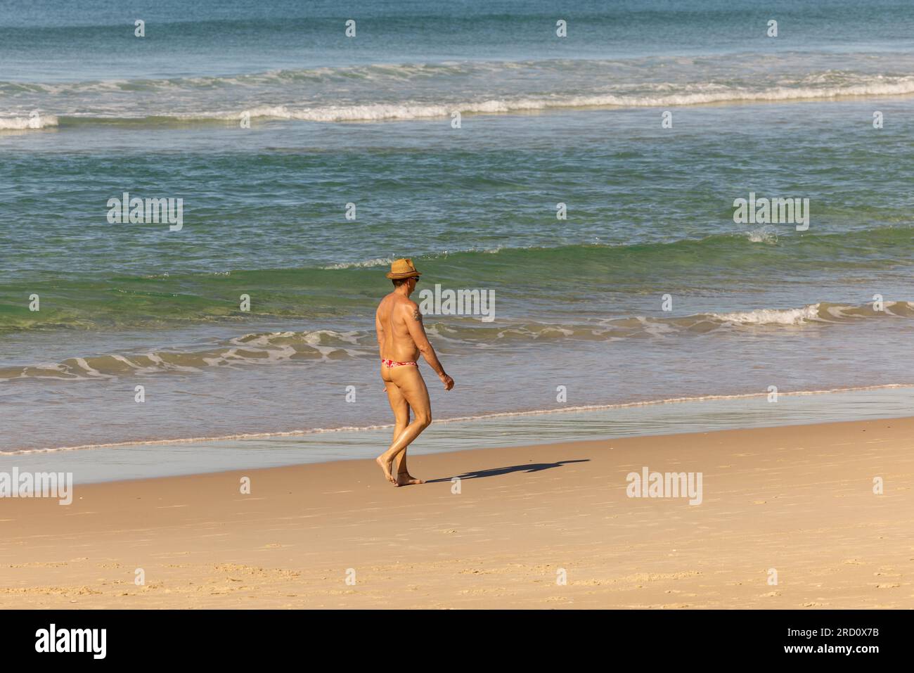 Uomo che cammina sulla spiaggia sulla Gold Coast, Queensland Australia, indossando un costume da bagno Foto Stock