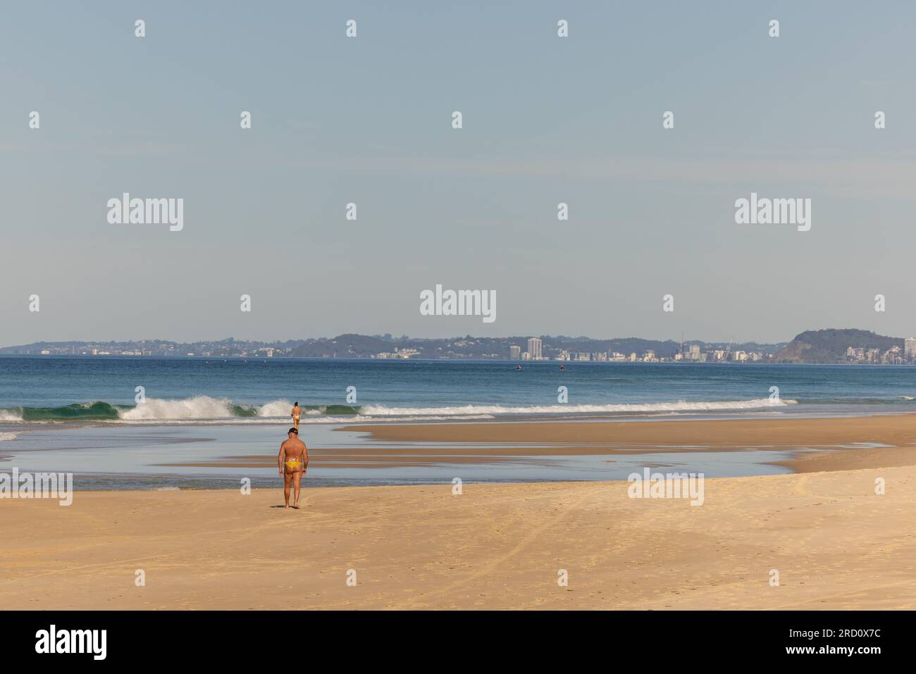 Uomo che cammina sulla spiaggia sulla Gold Coast, Queensland Australia, indossando un costume da bagno Foto Stock