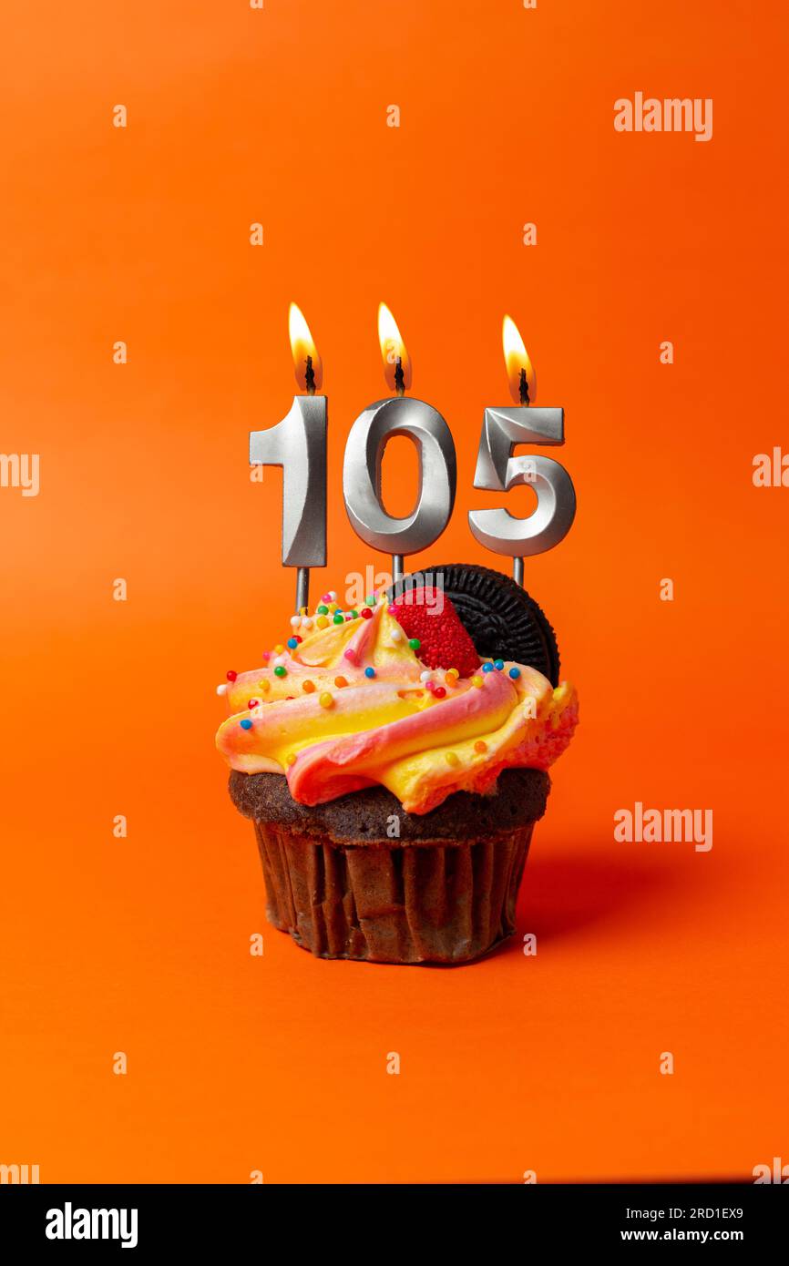 torta di compleanno con numero 105 - cupcake su sfondo arancione con candele di compleanno Foto Stock