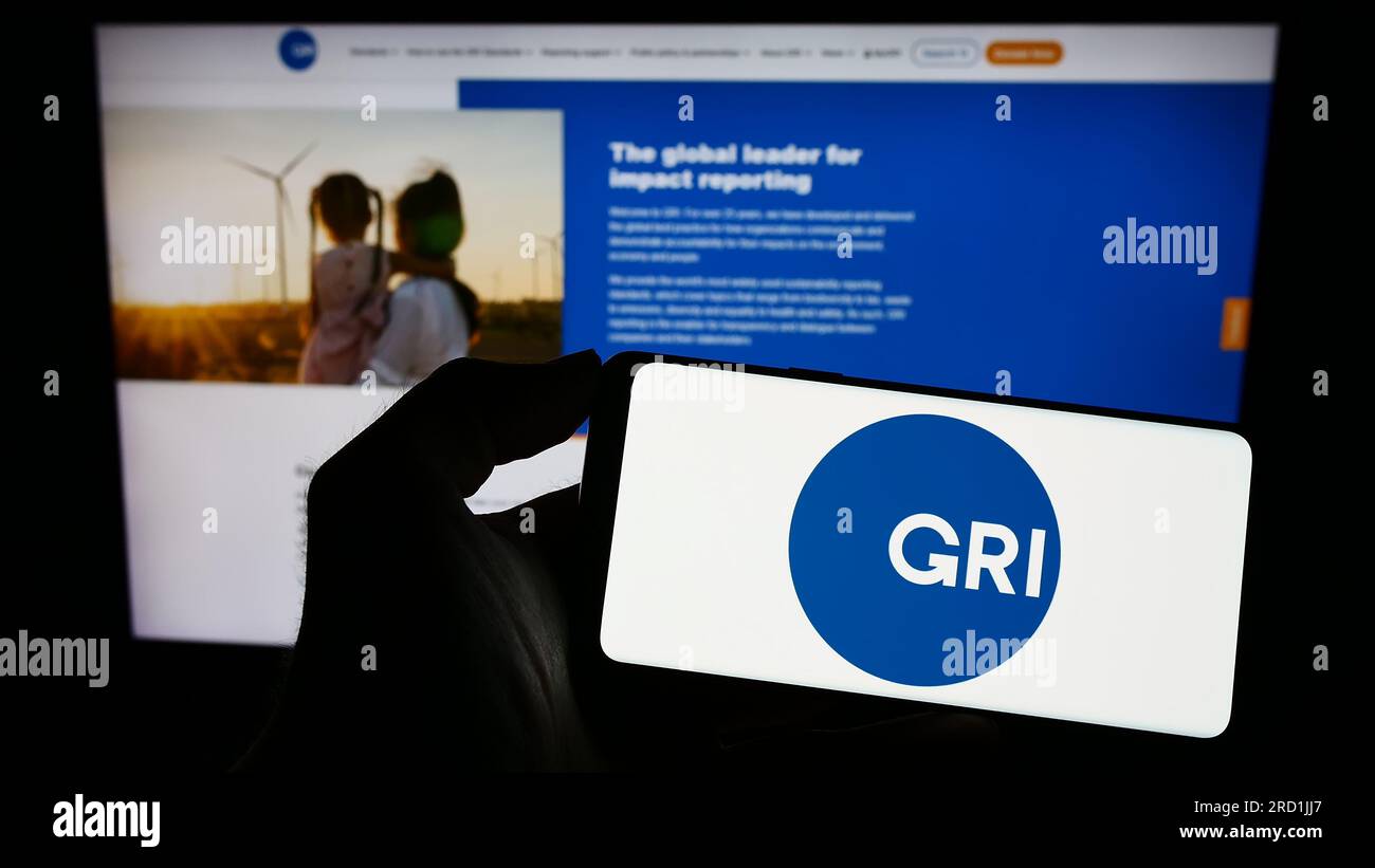 Persona che possiede un telefono cellulare con il logo della Global Reporting Initiative (GRI) sullo schermo davanti alla pagina Web. Concentrarsi sul display del telefono. Foto Stock