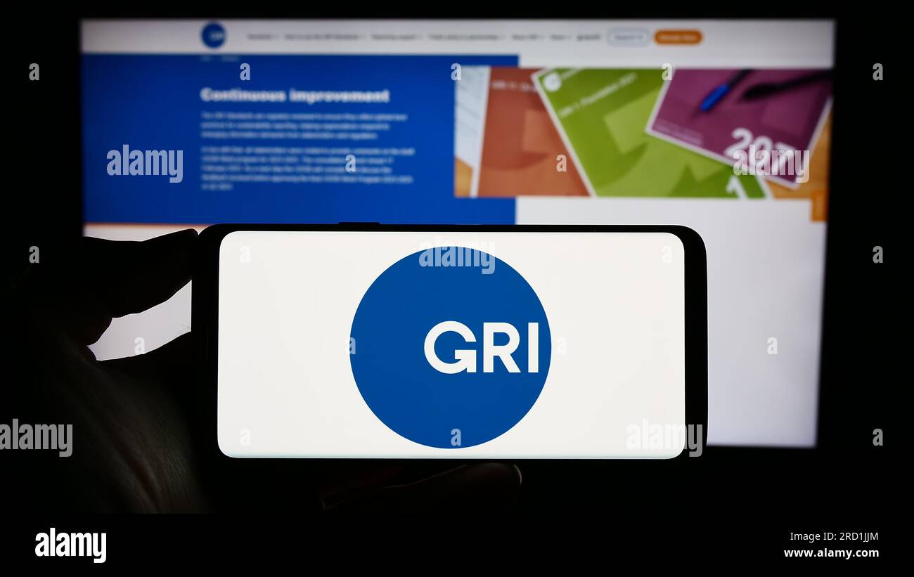 Persona in possesso di un cellulare con il logo della Global Reporting Initiative (GRI) sullo schermo davanti alla pagina Web. Concentrarsi sul display del telefono. Foto Stock