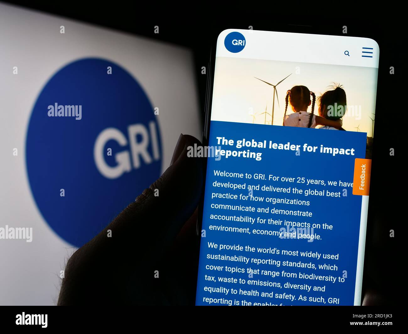 Persona in possesso di un cellulare con pagina Web della Global Reporting Initiative (GRI) sullo schermo davanti al logo. Concentrarsi sul centro del display del telefono. Foto Stock