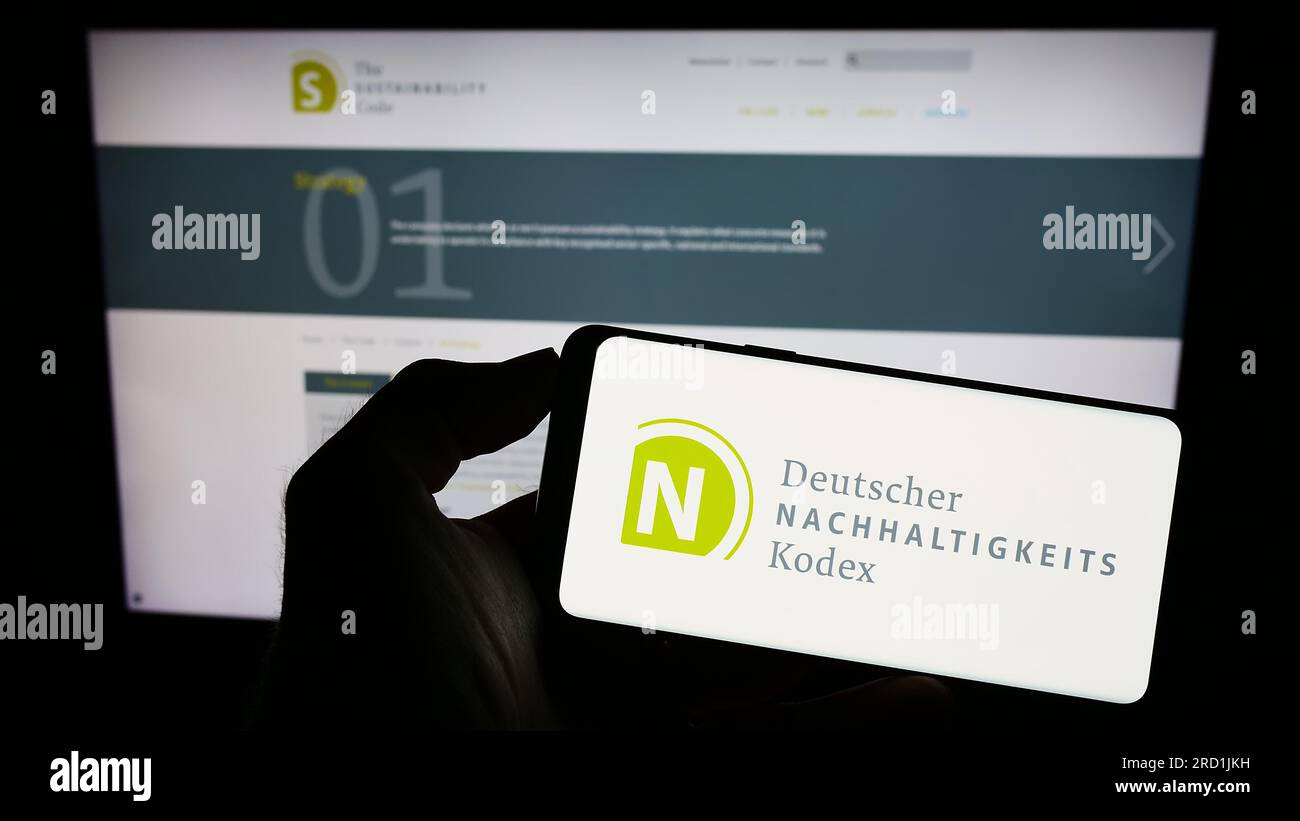 Persona che possiede il cellulare con il logo di Deutscher Nachhaltigkeitskodex (DNK) sullo schermo davanti alla pagina web. Concentrarsi sul display del telefono. Foto Stock