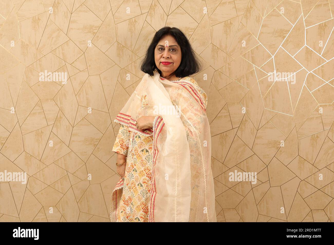 Vecchia signora indiana in piedi con il muro. Parete bianca. Bellissimo e felice ritratto della nonna in piedi contro il muro nel soggiorno arredato di recente. Foto Stock