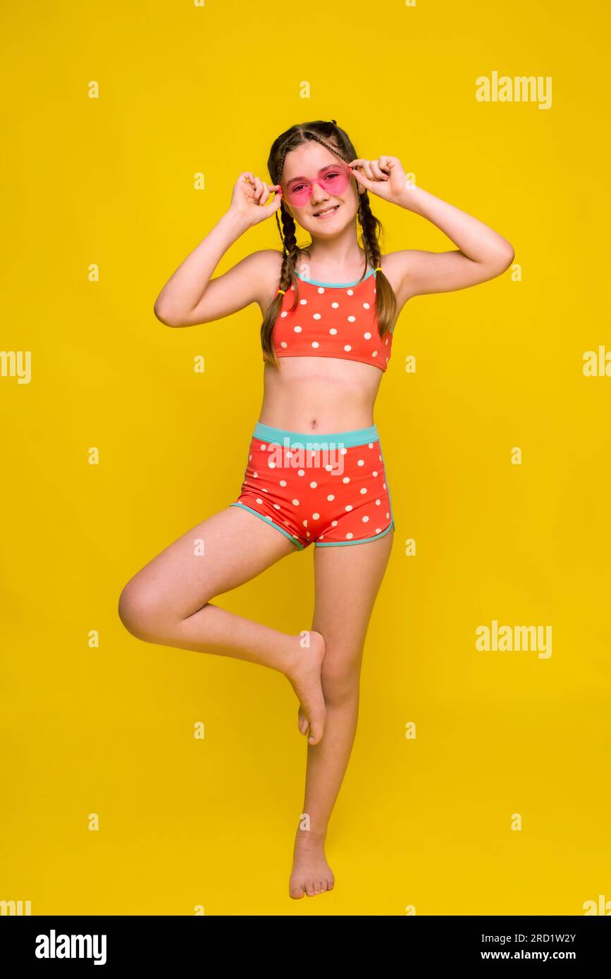 Simpatica ragazza sorridente che guarda la fotocamera in posa su una gamba su uno sfondo giallo brillante in studio Foto Stock
