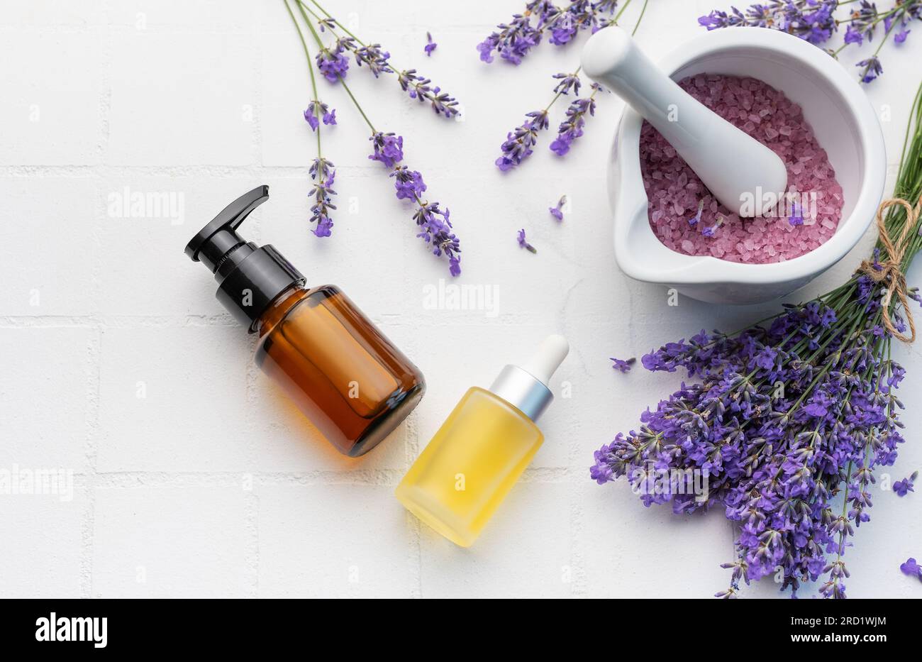 Vasca idromassaggio con lavanda. Sale di lavanda, olio essenziale naturale e lavanda fresca su fondo di piastrelle bianche. Foto Stock