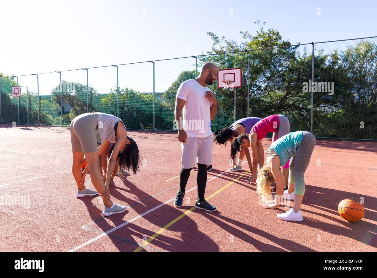 Diversi gruppi di donne con allenatore maschile che si allunga e si riscalda sul campo da pallacanestro Foto Stock
