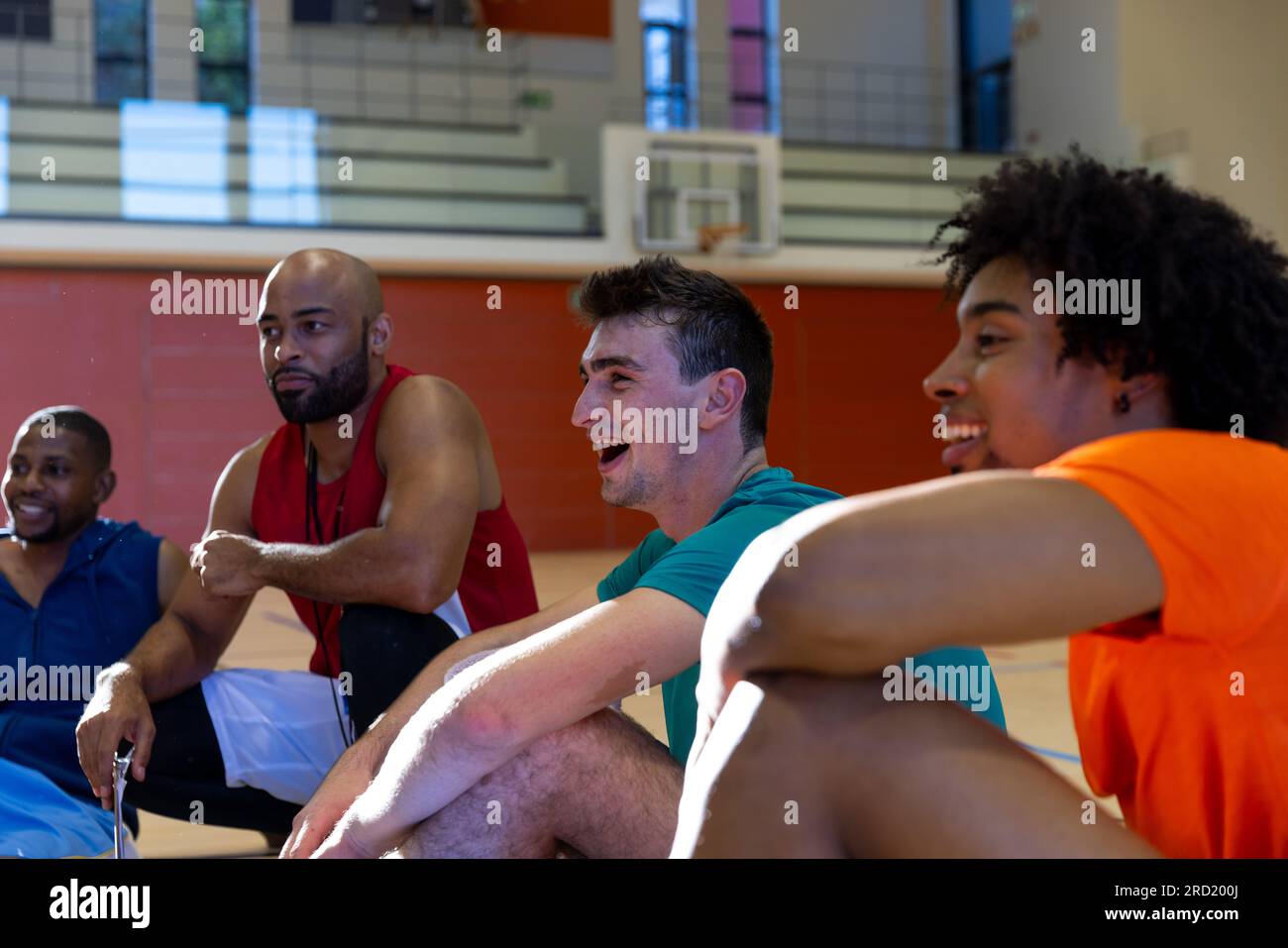 Divertiti con diversi giocatori di basket maschi seduti e chiacchierando con il coach in palestra Foto Stock