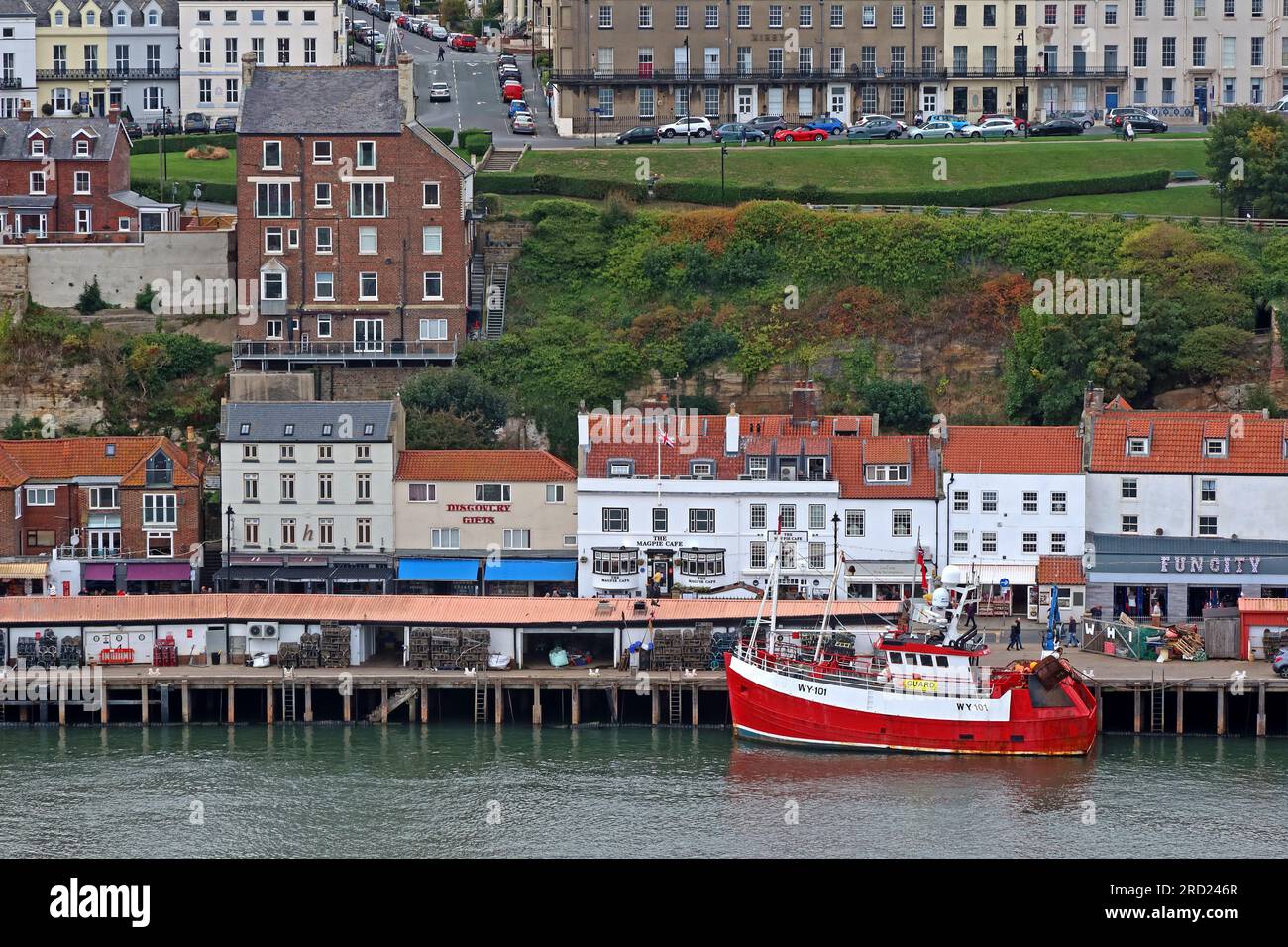 Vista di West Cliff, della città di Whitby, del porto e degli ormeggi, incluso un peschereccio rosso ormeggiato, North Yorkshire, Inghilterra, Regno Unito, YO21 3PU Foto Stock