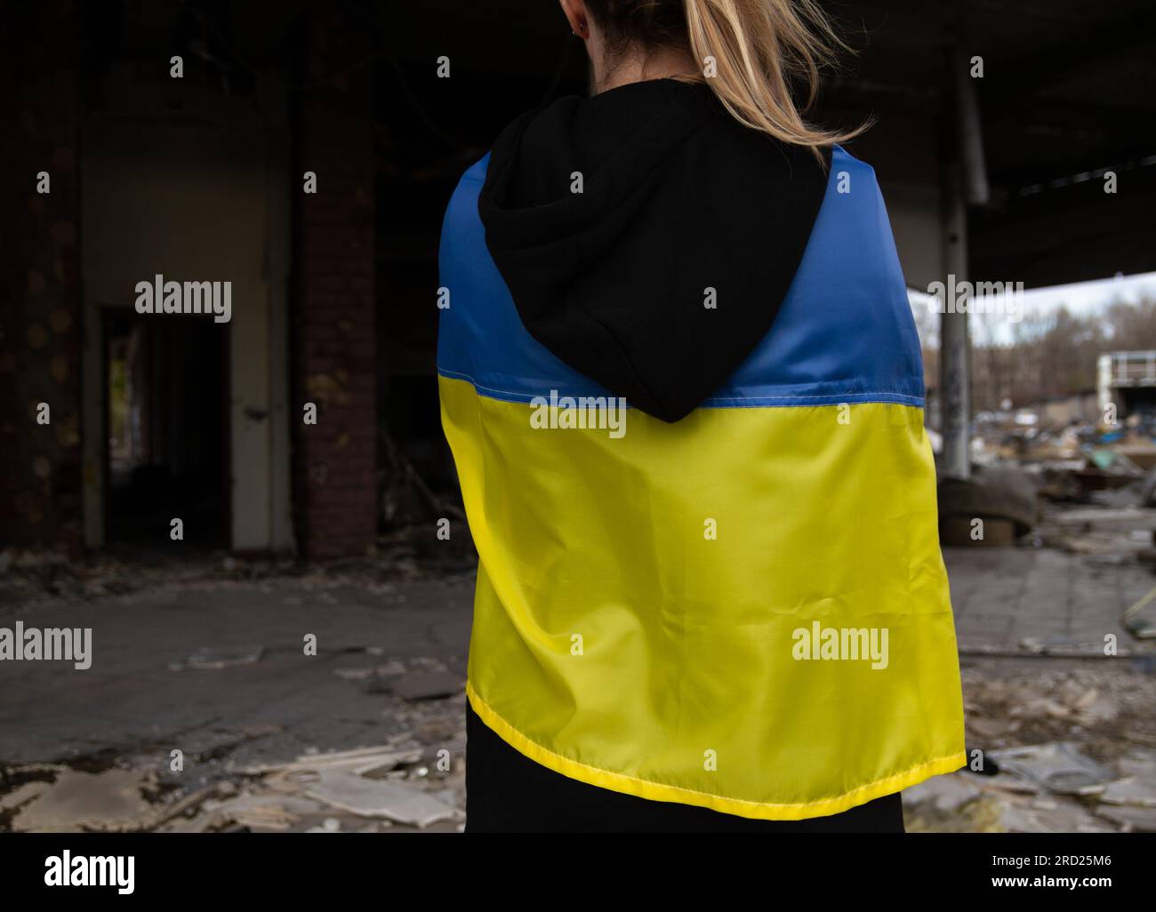 Donna con bandiera Ucraina che guarda l'edificio abbandonato distrutto. Invasione della Russia, guerra in Ucraina crisi. Ragazza di fronte alla casa distrutta e bombardata. Foto Stock