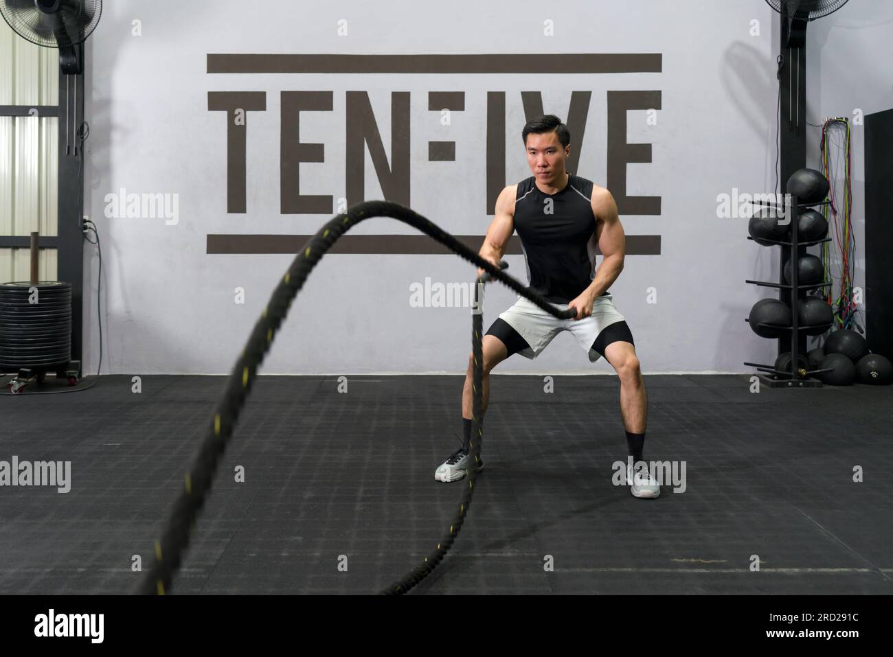 Ragazzo determinato che usa la corda mentre fa l'allenamento fisico. Giovane uomo forte che lavora con le corde in palestra. Atleta muscoloso che fa cross Excursion con Foto Stock
