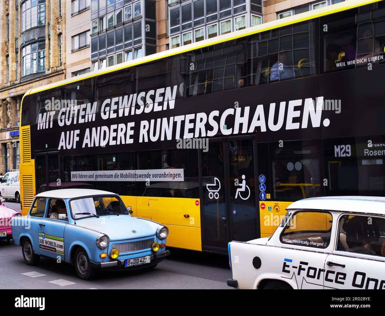 Berlino, Germania. 6 luglio 2023. 06.07.2023, Berlino. Su un autobus della società di trasporti pubblici berlinese BVG, un autobus a due piani con un secondo piano, si può leggere lo slogan pubblicitario "guardare in basso gli altri con la coscienza pulita”. BVG è nota per la sua pubblicità creativa e spiritosa con umorismo, cuore e ruggito. In primo piano ci sono le auto del cosiddetto "Trabbi-Safari", con le quali i turisti possono fare escursioni a Berlino. Credito: Wolfram Steinberg/dpa credito: Wolfram Steinberg/dpa/Alamy Live News Foto Stock