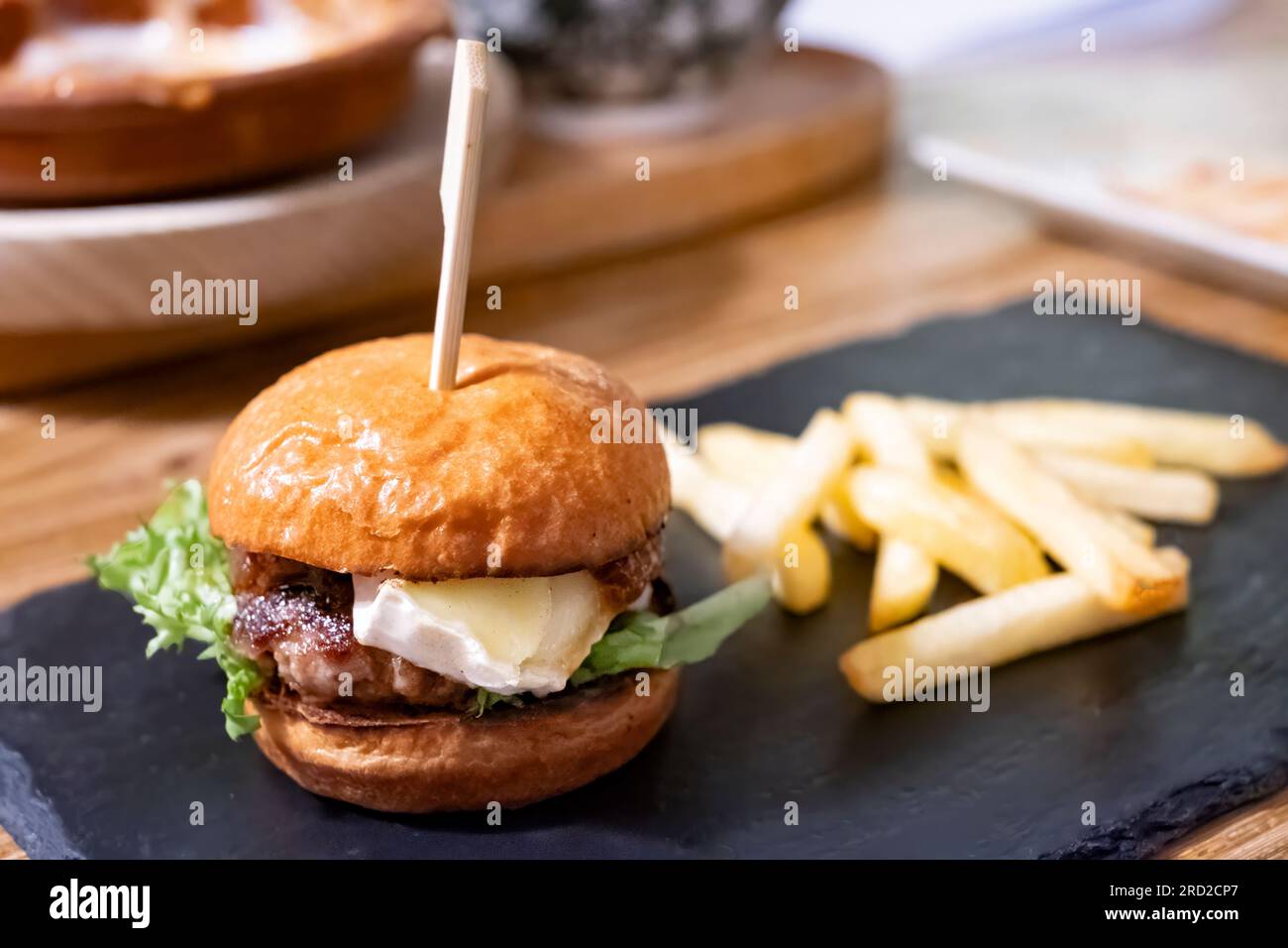 Un'unica porzione di Tapas di un piccolo hamburger di manzo condito con formaggio brie servito con patatine fritte in un Tapas bar. Foto Stock