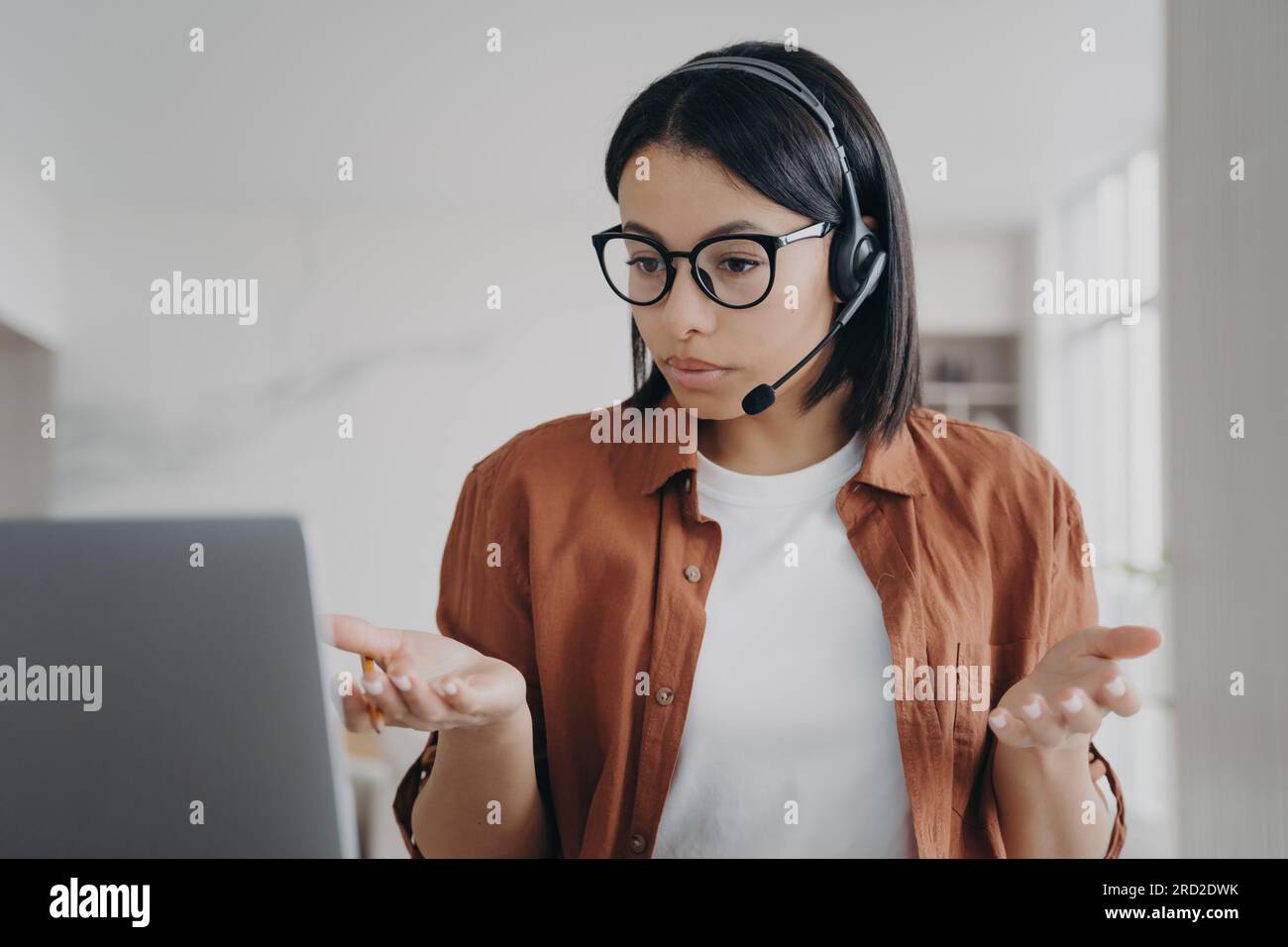 La giovane donna europea ha una conferenza online. Una donna d'affari con cuffie e occhiali sta parlando. Il manager o l'assistente aziendale è seduto alla scrivania e. Foto Stock