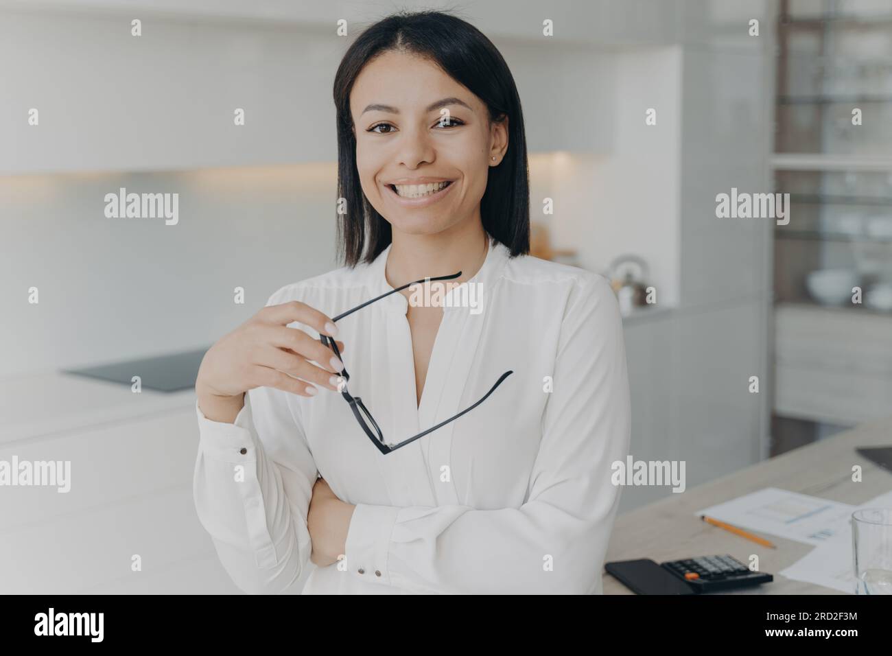 Ritratto di una felice imprenditrice in piedi in un ufficio moderno. Una donna d'affari professionista sorridente di mezza età che regge occhiali che guarda la camma Foto Stock