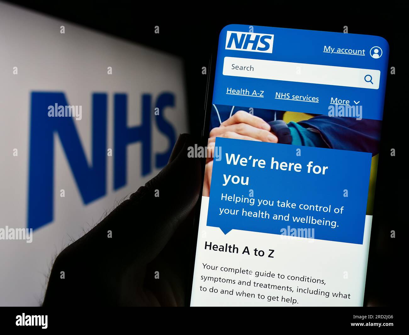 Persona che tiene lo smartphone con la pagina web del British National Health Service (NHS) sullo schermo davanti al logo. Concentrarsi sul centro del display del telefono. Foto Stock